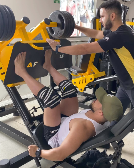 Personal trainer acompanhando aluno em equipamento